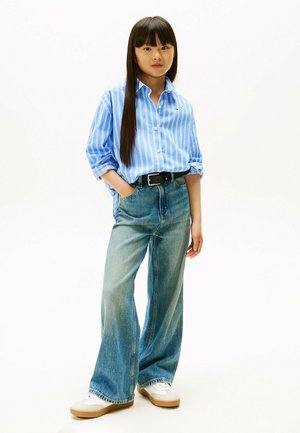 Blå og hvid stribet skjorte med knapper, afslappet pasform, parret med løse, lyse denim jeans og grå sneakers med beige detaljer.