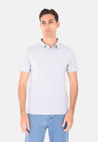 Polo grigio a maniche corte con colletto, chiusura a due bottoni e motivo a maglia testurizzato, abbinato a jeans azzurri chiari.