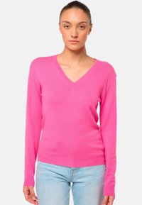 Rosa V-Ausschnitt-Pullover aus weichem Strickmaterial mit langen Ärmeln und Rippbündchen. Getragen mit hellblauen Jeans für den Kontrast.