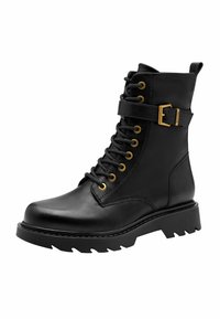 Stivaletto in pelle nera con occhielli dorati, cinturino decorativo e fibbia. Superficie testurizzata e suola in gomma spessa con battistrada pronunciato.
