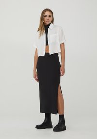 Camicia bianca tagliata, abito nero aderente con spacco laterale e stivali neri alla caviglia con suola spessa. Tessuto morbido e design strutturato.