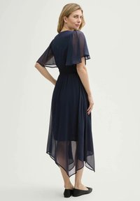Navyblaues Chiffonkleid mit kurzen, flatternden Ärmeln, gerafftem Taillenbereich und asymmetrischem Saum. Getragen mit schwarzen Ballerinas. Minimalistisches Design.