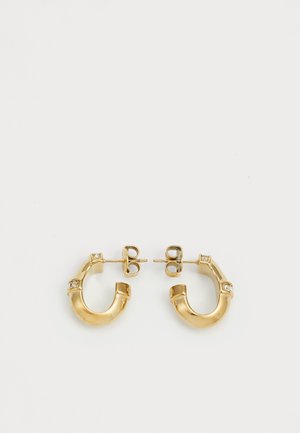 Boucles d'oreilles en or en forme de C, ornées de petites pierres claires disposées par intervalles. Leur texture lisse et leur finition brillante accentuent leur design.