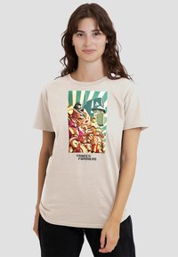 Beige T-Shirt mit einem Grafikmotiv von Robotern in Farben wie Rot und Gelb, mit grünen Streifen im Hintergrund und dem Text "Transformers" darunter.