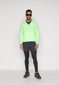 Νεον πράσινο φούτερ με φερμουάρ και κουκούλα, μαύρο αθλητικό μπλουζάκι, μαύρες βερμούδες και μαύρα κολάν. Μαύρα αθλητικά παπούτσια ολοκληρώνουν την αθλητική εμφάνιση.