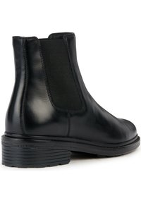 Botín de cuero negro con una superficie lisa, paneles laterales elásticos y un tacón de goma apilado. Presenta una punta redondeada y sin herrajes visibles.