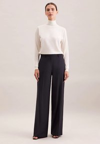 Biała bluzka z długim rękawem i golfem, zestawiona z czarnymi spodniami o szerokich nogawkach, wykonana z gładkiego materiału i o dopasowanym kroju. Brak widocznych wzorów czy zdobień.