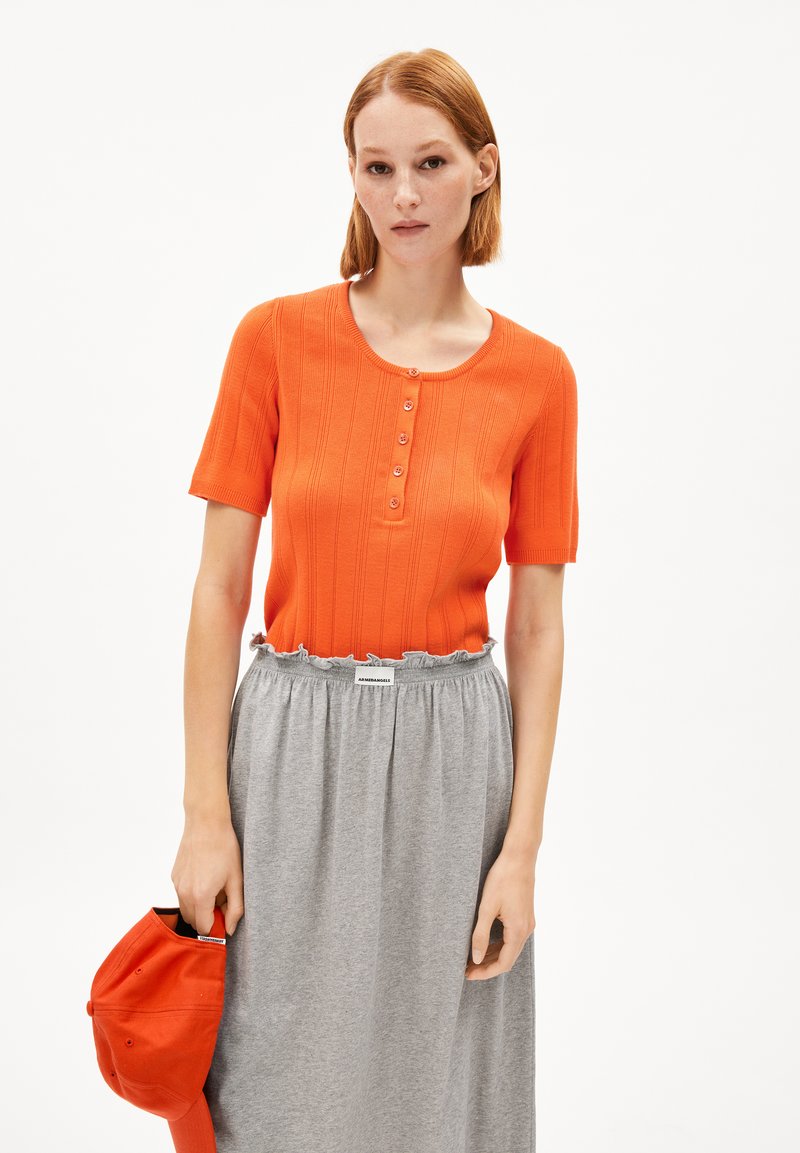 Haut court à manches courtes orange à côtes avec un col rond et un détail de bouton, associé à une jupe grise à taille froncée et une casquette orange.