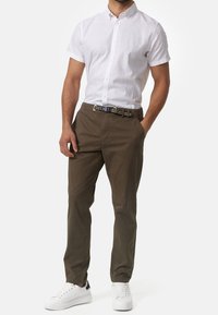 Kurzärmliges weißes Hemd mit Knöpfen, kombiniert mit olivgrünen Hosen und weißen Turnschuhen, dazu ein Gürtel mit schwarzen und grauen Streifen.