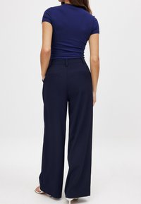 Tumed laiad püksid sujuva tekstuuriga, kahe taga taskuga ja kohandatud lõikega. Ühildatud sobiva lühikeste varrukatega tumeda pealisega.