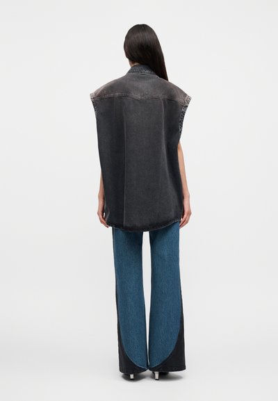 Υπερμεγέθη μαύρο τζιν γιλέκο με ακατέργαστες άκρες, σχεδιασμό χωρίς μανίκια και ασημένια ραφή. Συνδυάζεται με μπλε τζιν παντελόνια φαρδιάς γραμμής με καμπυλωτό διακοσμητικό στοιχείο.