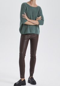 Oversized green knit sweater with three-quarter sleeves, paired with brown faux leather leggings and black loafers with chunky soles.