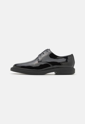 Chaussure de ville en cuir noir brillant à lacets, bout rond et petit talon, vue de profil sur fond blanc uni.