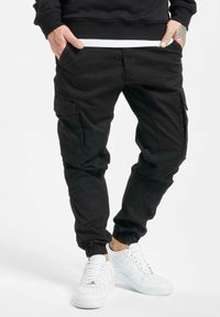 Pantalon cargo noir avec poignets élastiques, poches latérales et coupe décontractée, associé à des baskets blanches avec des détails perforés.