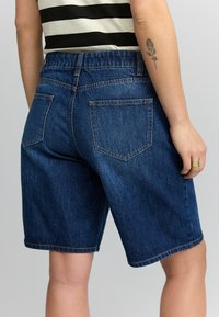 Pantalones cortos de mezclilla en azul oscuro con un corte relajado, que presentan una cintura elástica, cinco bolsillos y un dobladillo que se sitúa por encima de la rodilla.