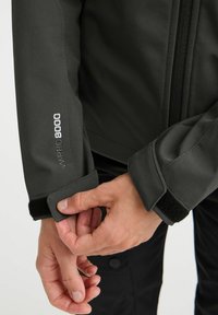 Mørkegrå jakke med lommer, glidelås foran, justerbare mansjetter med borrelås, og "WPRO 8000" brodert på ermet i hvit tråd.