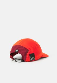Rød og oransje løpecaps med en svart og burgunder bakdel. Har en vevd tekstur, justerbar stropp og et logomerke på siden.
