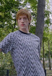 Camiseta de manga corta y cuello redondo en blanco y negro, con un patrón repetido del logo "Levi's". Hecha de un suave material de algodón.