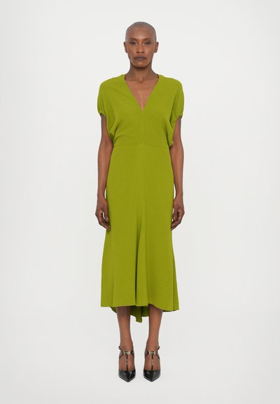 Robe verte à manches courtes avec un décolleté en V, un corsage ajusté et une jupe évasée. Texture lisse, longueur genou avec un dos légèrement plus long.