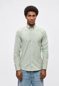 Πουκάμισο με μακριά μανίκια, ανοιχτοπράσινο, με κουμπιά και γιακά, κατασκευασμένο από υφασμένο ύφασμα, σε συνδυασμό με ξεθωριασμένο μπλε τζιν.