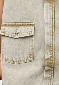 Gilet in denim beige con tasca sul petto, dotato di chiusura con bottoni automatici in argento, leggera usura e cuciture a vista.