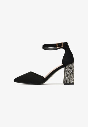 Décolleté nera con tacco alto, punta a punta e cinturino alla caviglia. Presenta un motivo strutturato sul tacco a blocco. Realizzata in suede e materiali sintetici.