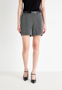 Shorts en tweed gris avec un léger brillant, dotés d'une ceinture noire, de poches latérales et d'une coupe droite. Associés avec des escarpins noirs à bout pointu.