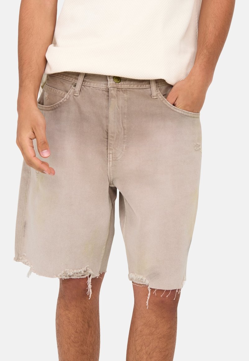 Shorts de mezclilla beige con dobladillo deshilachado, diseño de cinco bolsillos y un ligero desgaste. Botón dorado en la cintura, livianos y con un ajuste casual.