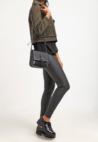 Giacca corta oliva, top nero, leggings in pelle nera lucida, scarpe con plateau nere e una piccola borsa a tracolla nera. Design semplice e moderno.