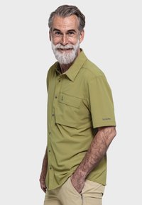 Kurzärmliges grünes Hemd mit Knopfleiste, ausgestattet mit einer Fronttasche, grauen Knöpfen und einem Logo auf dem Ärmel. Glatte Textur.