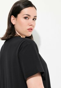 Mustat lyhythihaiset t-paidat, joissa on pyöreä pääntie, esiteltynä sivusta, sileä rakenne, minimalistinen muotoilu ja standardi istuvuus.