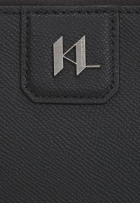 Sort tekstureret læderpung med et sølvmetallogo med "K" og L. Detaljeret syning og et hævet logo på en sidepatch.