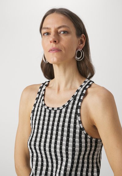 Svart og hvit stripete tank top med rund hals, med teksturert stoff og knutede detaljer på stroppene. Sølv hoop-øreringer.