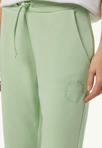 Helle grüne Jogginghose aus weichem, strukturiertem Stoff. Verfügt über Seitentaschen und ein besticktes rundes Design mit dem Text "POSITIVE VIBES."
