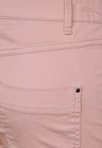 Ljusrosa denimtyg med en slät textur, med en bakficka försedel med en svart nitarknapp och synliga sömdetaljer.