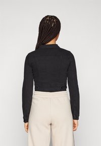 Černá zkrácená džínová bunda s dlouhými rukávy, knoflíkovými manžetami a plochým límcem. Má šité detaily na zadní straně a strukturovaný střih.