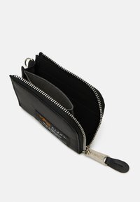 Portefeuille en tissu noir avec fermeture éclair argentée, plusieurs emplacements pour cartes et une surface texturée. Équipé d'un patch logo et d'une tirette en cuir.