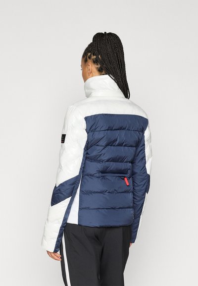 Μπουφάν με επένδυση που διαθέτει γυαλιστερό σχέδιο σε λευκό και ναυτικό χρώμα, ψηλό κολάρο και πίσω τσέπη με κόκκινη λεπτομέρεια. Υφή με κομμάτια σε κουβαρδιστό σχέδιο.