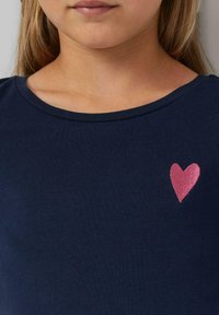 Navyblaues Baumwoll-T-Shirt mit Rundhalsausschnitt und kurzen Ärmeln, das auf der linken Seite ein pinkes gesticktes Herz zeigt. Glatte Textur.
