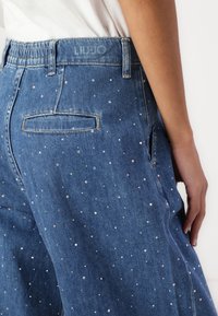 Blauwe spijkerbroeken met een losse pasvorm, versierd met verspreide heldere rhinestones en een elastische tailleband. Merkl logo zichtbaar op de achterkant.