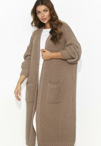 Dzianinowy kardigan w jasnobrązowym kolorze z teksturowanym wzorem, o za dużych rękawach i dwóch przednich kieszeniach, zaprojektowany z myślą o komforcie i cieple.