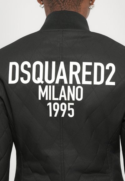 Giacca bomber nera trapuntata con colletto a coste. Presenta un grande testo bianco: "DSQUARED2 MILANO 1995" sul retro. Design semplice e moderno.