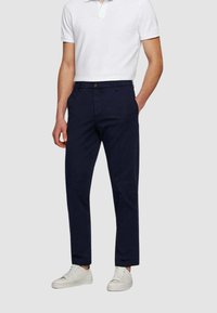 Chino blu navy realizzati in misto cotone, con design a gamba dritta, tasche frontali e chiusura con bottone, abbinati a sneaker bianche.