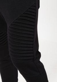 Pantalones jogger negros con textura acanalada a lo largo de los lados, material suave, diseño ajustado y panel en contraste en un diseño elegante.