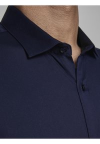 Tmavě modrá košile s límečkem zblízka, se smooth texturou, detaily knoflíků a čistým, strukturovaným výstřihem.