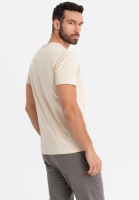 Camiseta de algodón beige de manga corta, con cuello redondo y una textura suave. El ajuste es casual, diseñado para la comodidad.