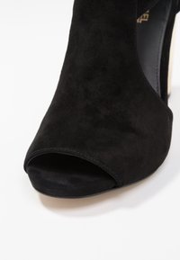 Mustat mokkanahkakenkiä, joissa on avonainen varvas, sileä pinta, voimakas kaari ja minimalistinen muotoilu, jossa on hienovarainen ommelreuna.