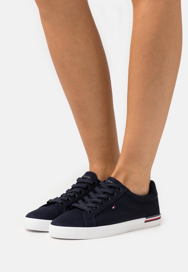 Baskets en toile marine avec semelles en caoutchouc blanches, bouts ronds et lacets plats. Présentant un petit logo accentué et un détail rayé sur le talon.