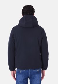 Giacca puffer blu scuro con cappuccio, caratterizzata da una texture liscia e polsini elasticizzati. La vista posteriore mostra un orlo arrotondato e un design minimale.