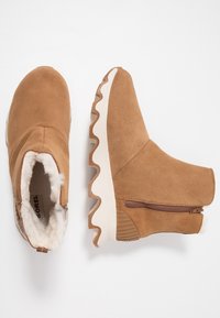 Brązowe zamszowe botki za kostkę z podszyciem ze sztucznego futra, rowkowaną podeszwą i bocznym zamkiem. Posiadają białą, falistą podeszwę środkową i zaokrąglony nosek.